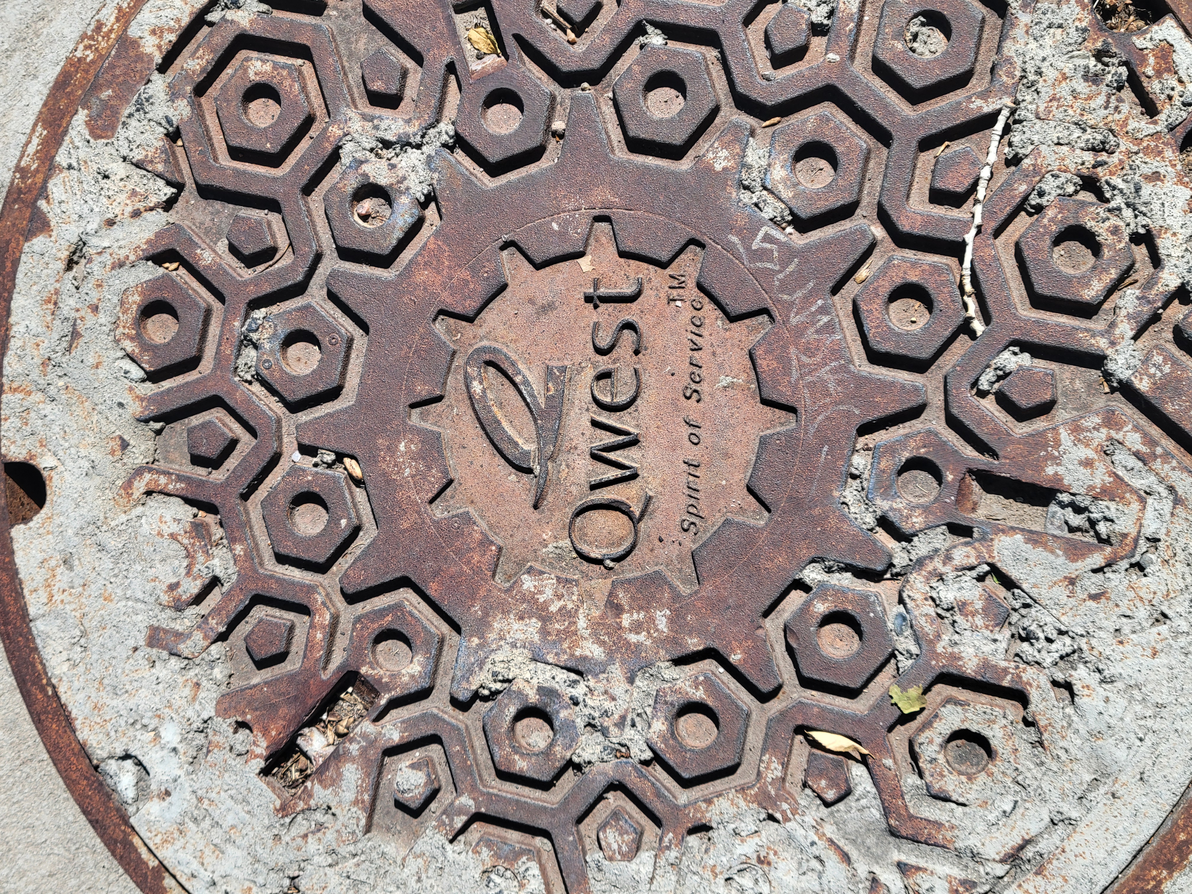 Sewage cover with the logo and motto of Qwest on it.